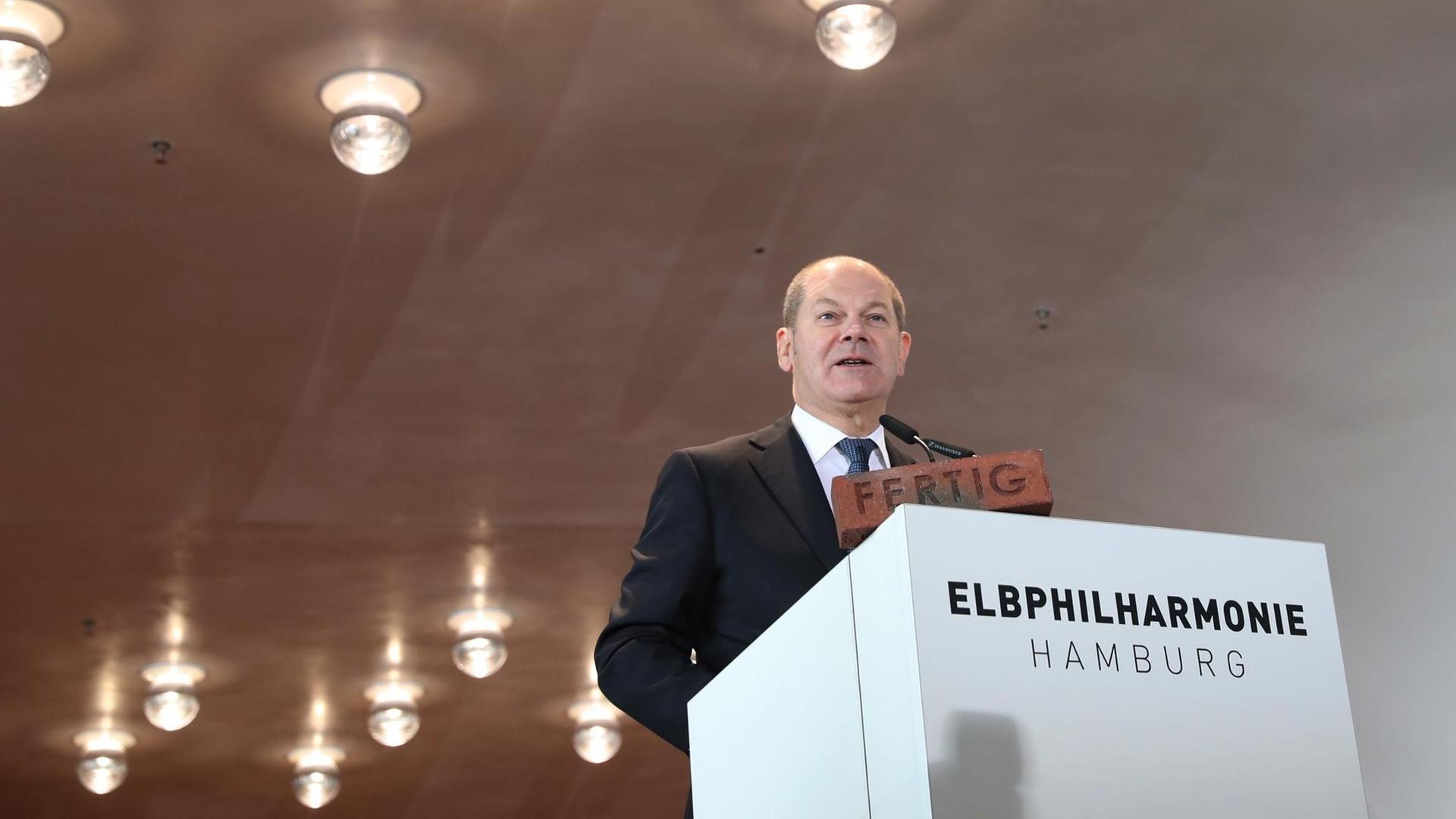 Hamburgs Erster Bürgermeister Olaf Scholz (SPD) steht vor einem weißen Pult mit der Aufschrift "Elbphilharmonie". Hamburgs Erster Bürgermeister Olaf Scholz (SPD) steht vor einem weißen Pult mit der Aufschrift "Elbphilharmonie".