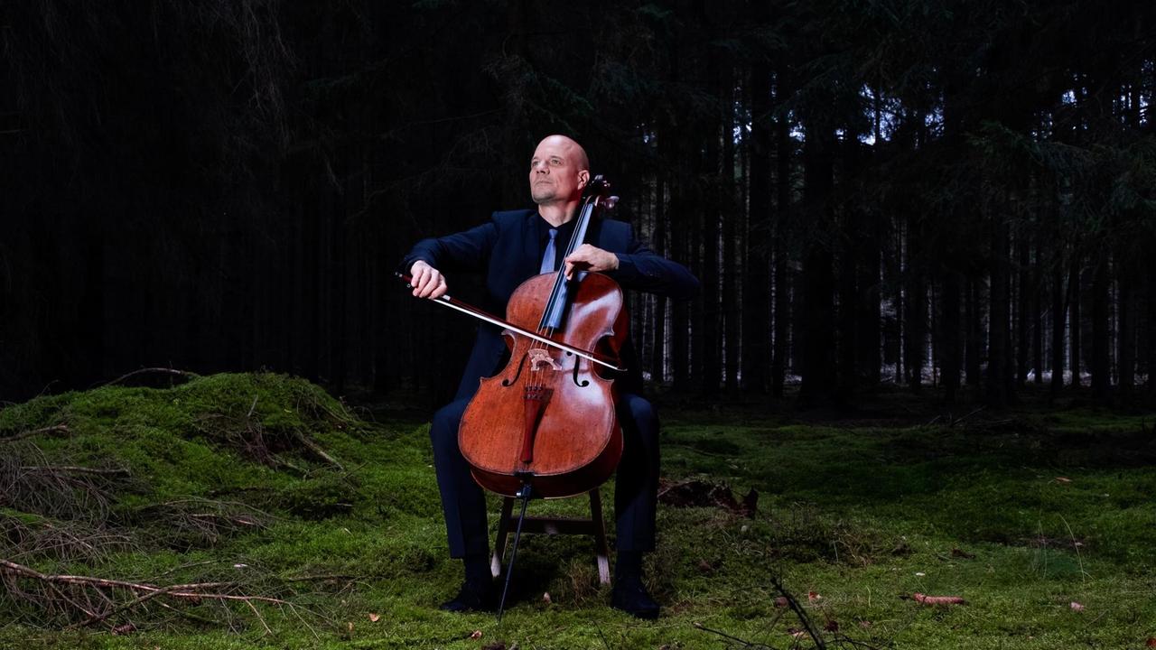 Eckart Runge spielt Cello auf einer kleinen Waldlichtung.