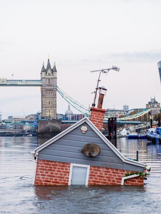 Ein nachgebildetes britisches Haus schwimmt, zur Hälfte im Wasser versunken, vor der Tower Bridge in der Themse. "Our house is flooding'" heisst die Kunstaktion der Umweltschutzgruppe Extinction Rebellion.