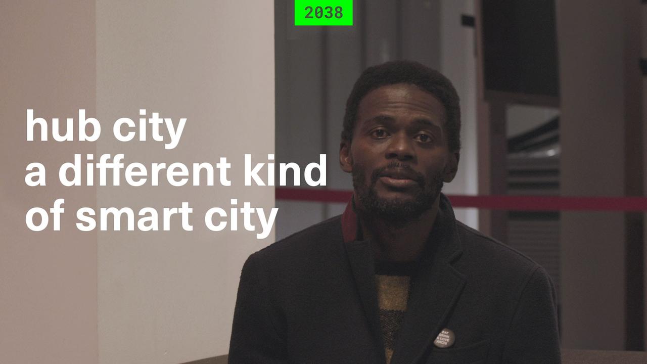 Still eines "2038"-Films: Ein Mann blickt in die Kamera. Daneben der Schriftzug: "hub city - a different kind of smart city". Still eines "2038"-Films: Ein Mann blickt in die Kamera. Daneben der Schriftzug: "hub city - a different kind of smart city".