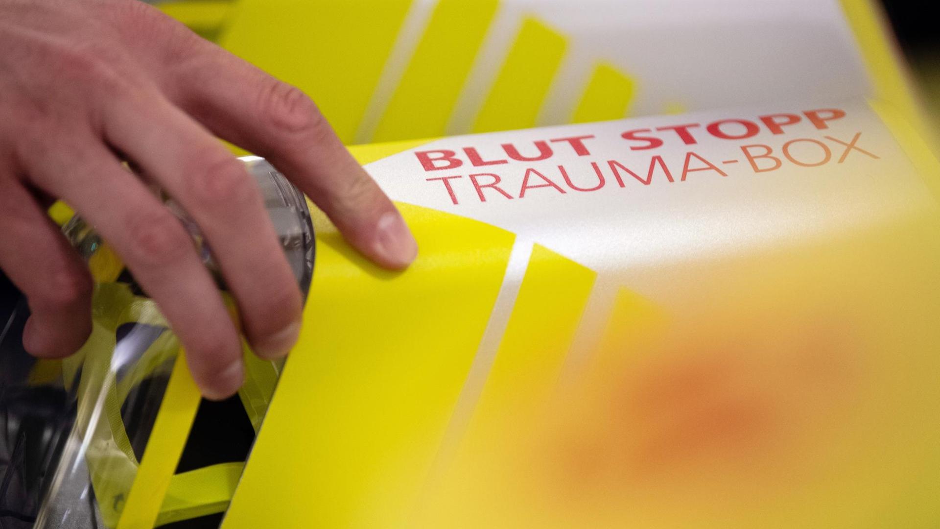 Eine Hand greift nach der Trauma-Box mit der Aufschrift «Blut Stopp». Die Box enthält ein sogenanntes Tourniquet, ein Abbindesystem ähnlich einer Blutdruckmanschette, und einen saugfähigen Druckverband zum Stillen einer Blutung eines Verletzten, bis medizinisches Fachpersonal eintrifft. Eine Hand greift nach der Trauma-Box mit der Aufschrift «Blut Stopp». Die Box enthält ein sogenanntes Tourniquet, ein Abbindesystem ähnlich einer Blutdruckmanschette, und einen saugfähigen Druckverband zum Stillen einer Blutung eines Verletzten, bis medizinisches Fachpersonal eintrifft.