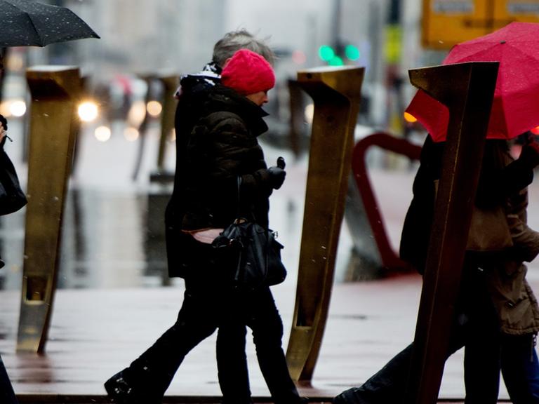 Passanten schützen sich am 10.12.2014 am Potsdamer Platz in Berlin mit Schirmen vor dem Regen.