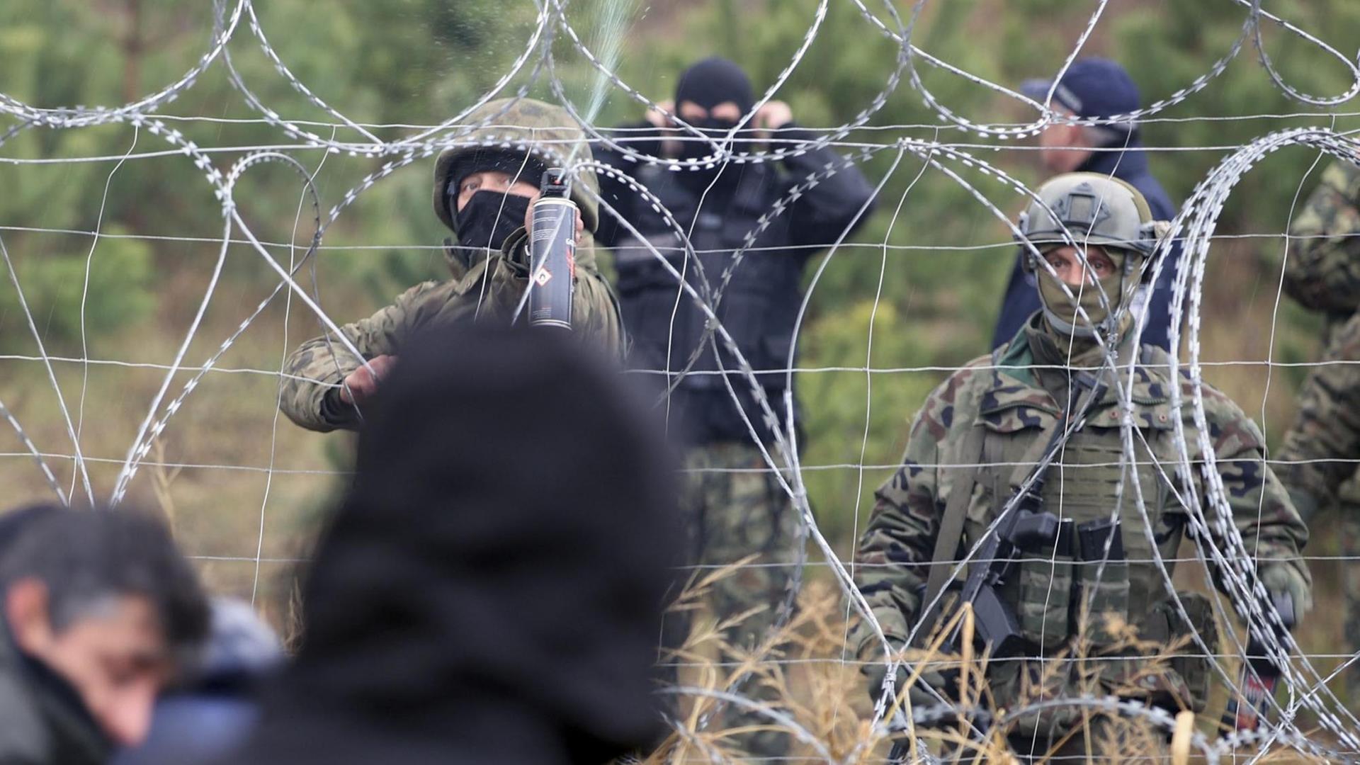 Polnische Grenzpolizisten stehen an einem Stacheldrahtzaun, hinter dem Migranten stehen. Polnische Grenzpolizisten stehen an einem Stacheldrahtzaun, hinter dem Migranten stehen.