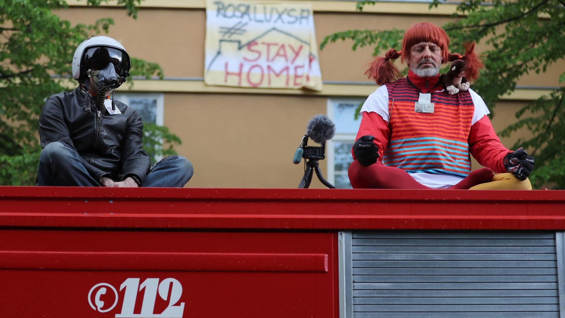 Zwei Demonstranten sitzten verkleidet auf einem ehemaligen Feuerwehrfahrzeug am Rosa-Luxemburg-Platz bei einer Kundgebung gegen die Corona-Einschränkungen.