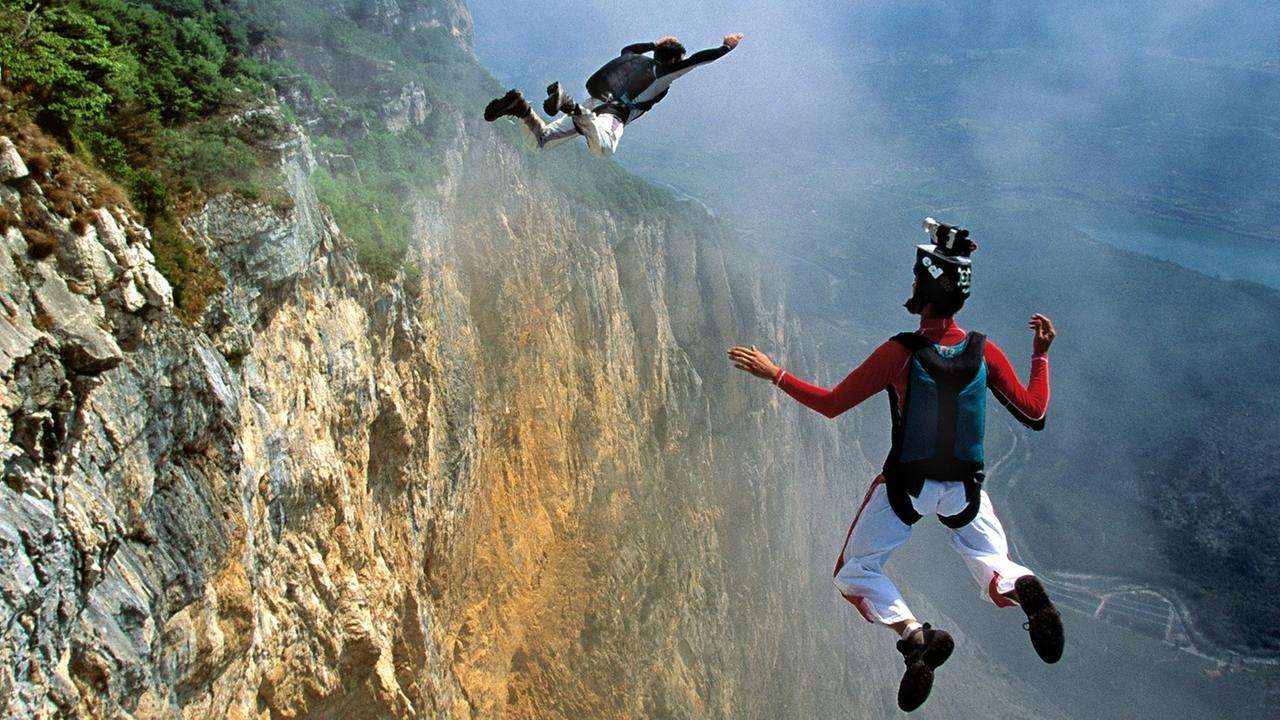 Zwei junge Männer springen als Basejumper von einem hohen Berg. Zwei junge Männer springen als Basejumper von einem hohen Berg.