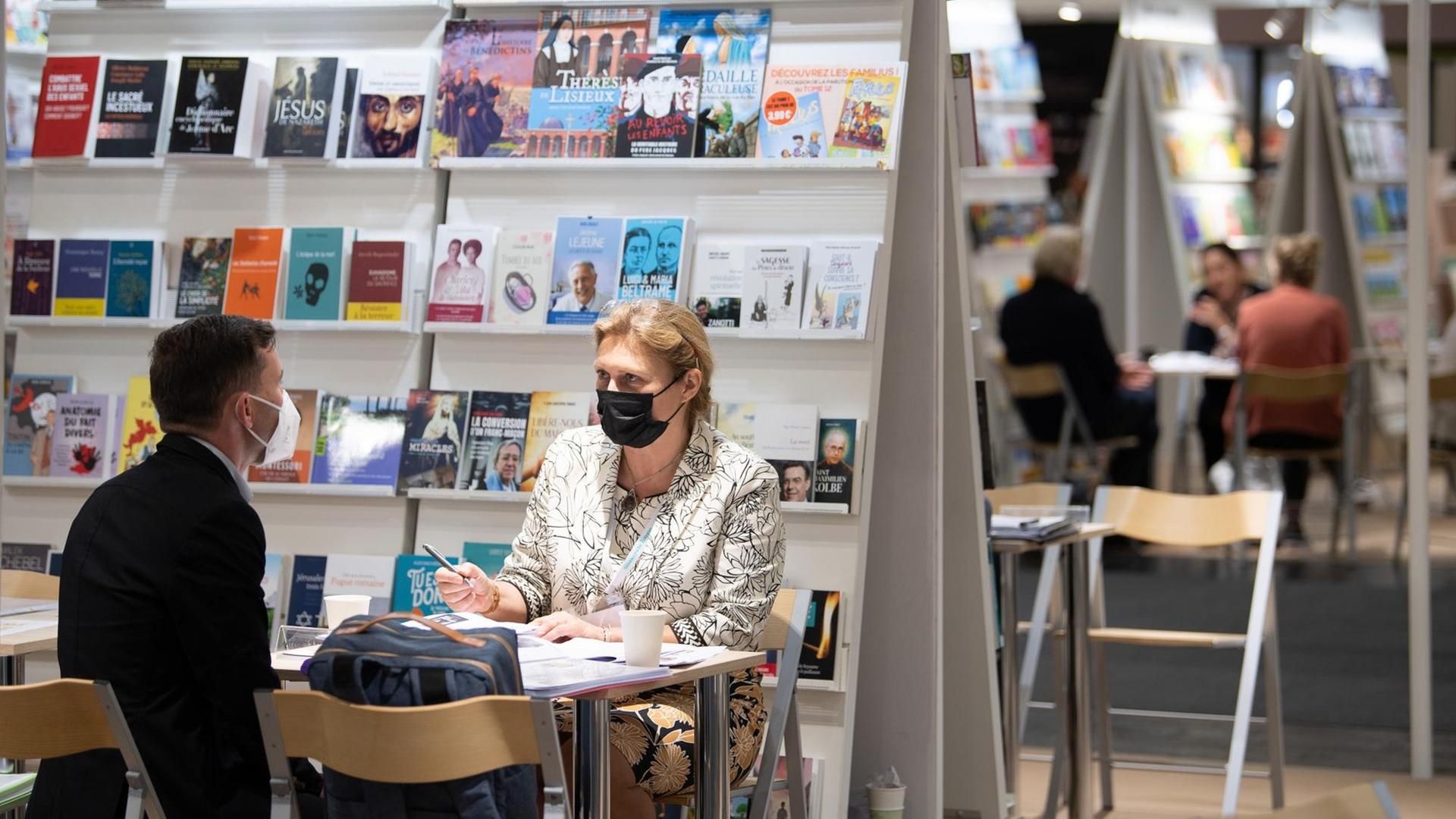 2 Mitarbeiter von Verlagen sprechen an einem Buch-Stand. 2 Mitarbeiter von Verlagen sprechen an einem Buch-Stand.