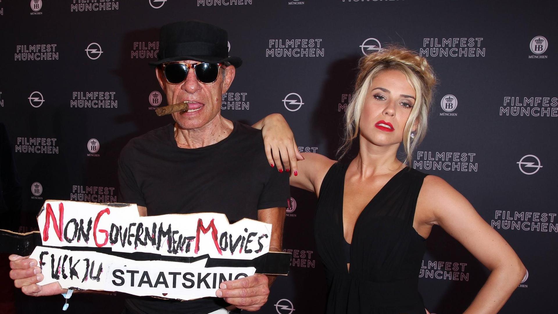 Klaus Lemke und Hauptdarstellerin Judith Paus bei der Eröffnung des Filmfests München im Mathaeser Filmpalast. Paus träge einen Hut, eine Sonnenbrille und hat eine Zigarre im Mund. In der Hand hält er ein Schild, auf dem steht: "Non Government Movies. Fuck ju Staatskino". Klaus Lemke und Hauptdarstellerin Judith Paus bei der Eröffnung des Filmfests München im Mathaeser Filmpalast. Paus träge einen Hut, eine Sonnenbrille und hat eine Zigarre im Mund. In der Hand hält er ein Schild, auf dem steht: "Non Government Movies. Fuck ju Staatskino".