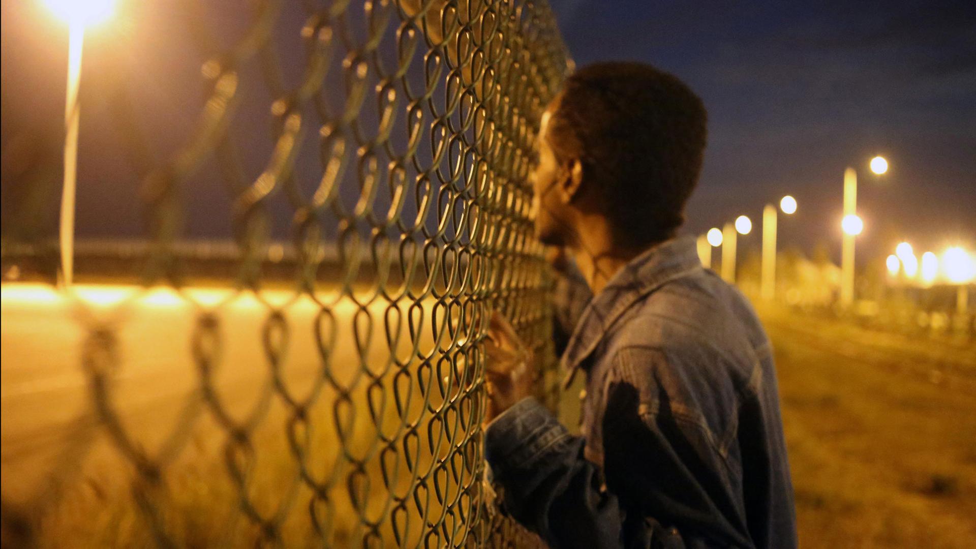 Ein Flüchtling schaut an der französischen Grenze durch einen Zaun.