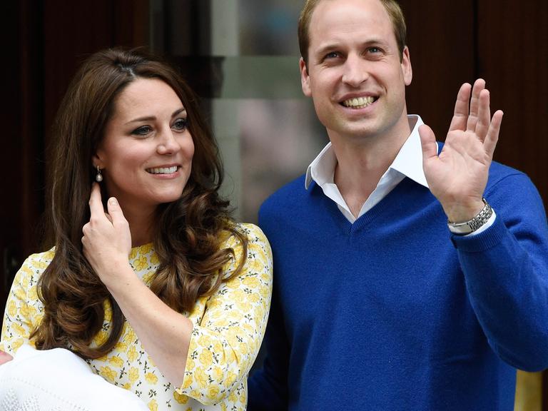 Kate hält das Baby in ihrem Arm, neben ihr William, der winkt.