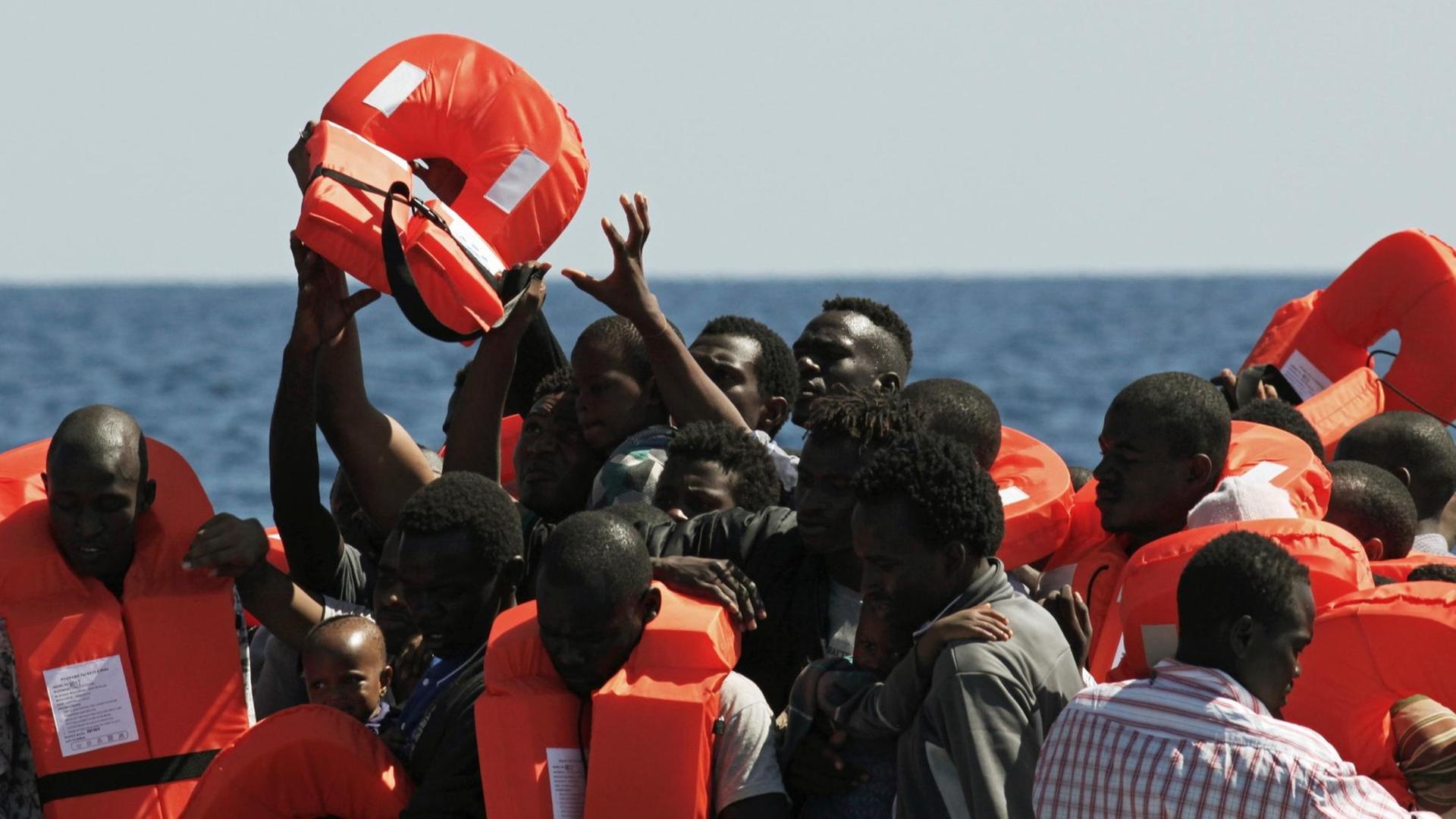 Mehrere Menschen greifen nach Rettungswesten, einige tragen bereits welche. Mehrere Menschen greifen nach Rettungswesten, einige tragen bereits welche.