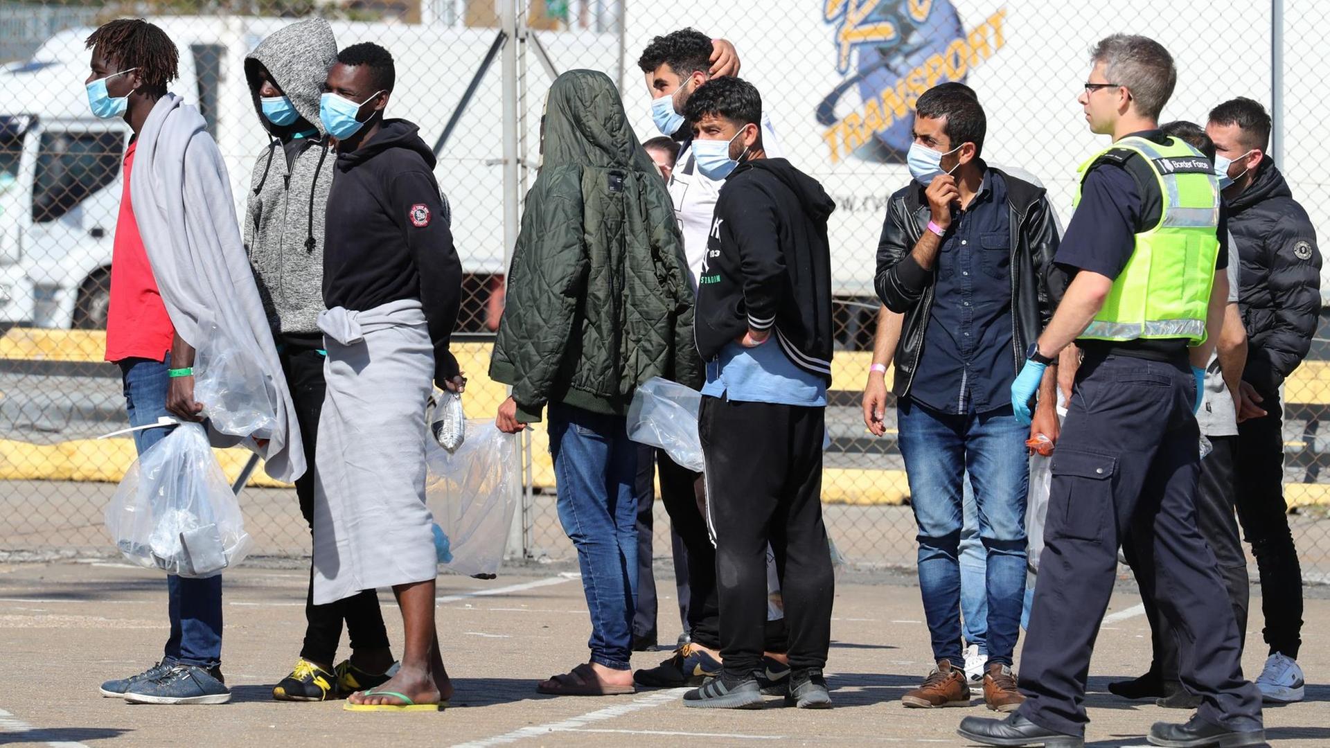 Dover: Beamte der Grenztruppen eskortieren eine Gruppe von Männern, mutmaßlich Migranten, zu einem wartenden Bus. Dover: Beamte der Grenztruppen eskortieren eine Gruppe von Männern, mutmaßlich Migranten, zu einem wartenden Bus.