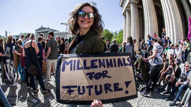 Eine Demonstrantin in München hält am Karfreitag ein Schild mit der Aufschrift "Millennials for Future" in die Kamera.