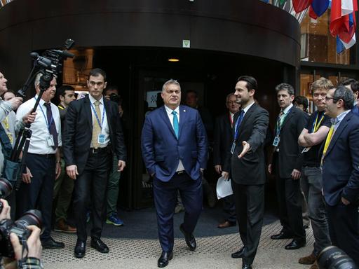 Ungarns Premierminister Victor Orbán verlässt nach einem Treffen des Europarates mit den Händen in den Hosentaschen ein Gebäude in Brüssel mit Fahnen europäischer Staaten über dem Eingang.
