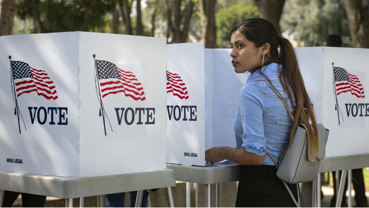 Eine junge Wählerin in den USA steht zwischen "Vote" Schildern. Eine junge Wählerin in den USA steht zwischen "Vote" Schildern.