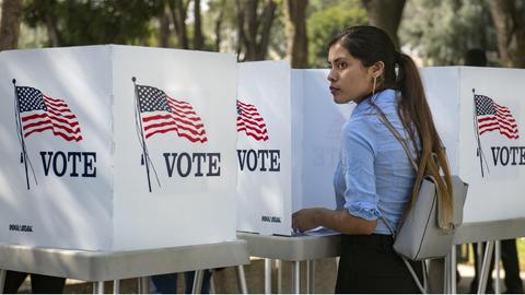 Eine junge Wählerin in den USA steht zwischen "Vote" Schildern.
