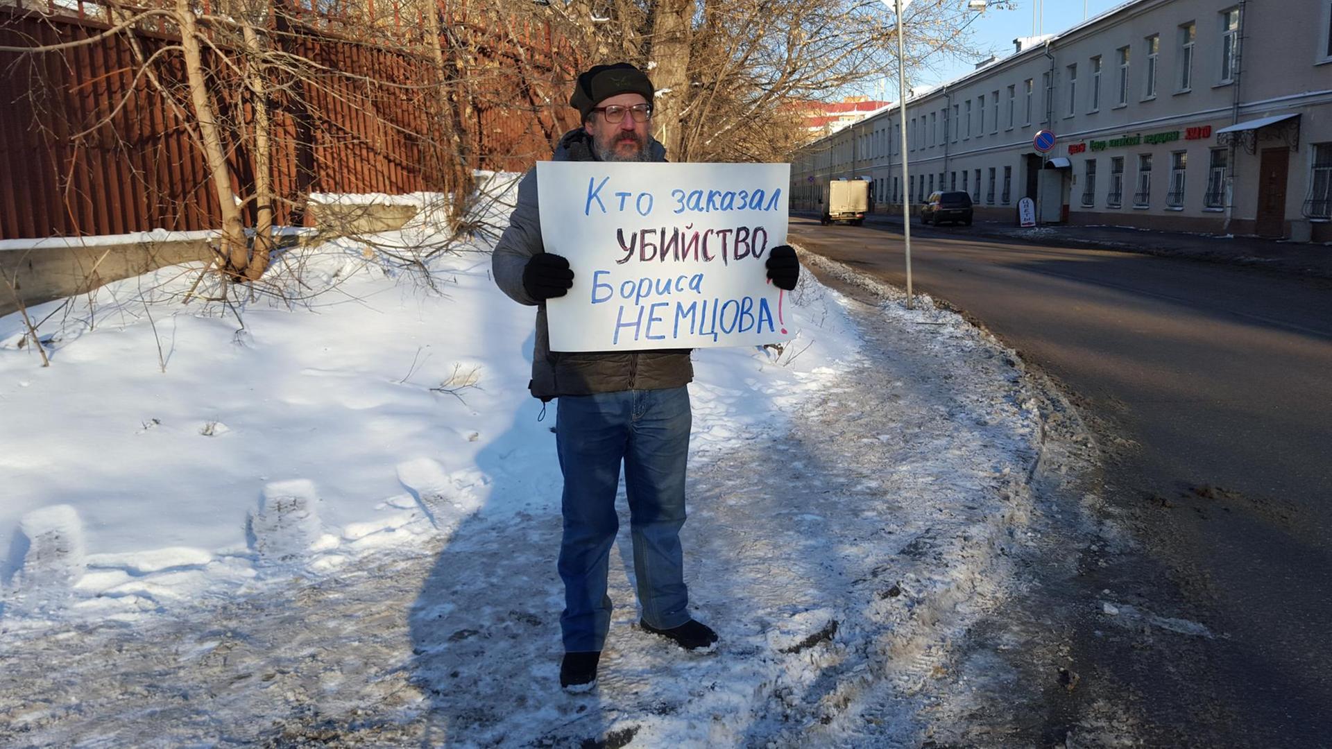 Ein Demonstrant vor dem Moskauer Militärgericht hält ein Schild hoch auf dem "Wer gab den Mord an Nemzow in Auftrag?" geschrieben steht. Ein Demonstrant vor dem Moskauer Militärgericht hält ein Schild hoch auf dem "Wer gab den Mord an Nemzow in Auftrag?" geschrieben steht.