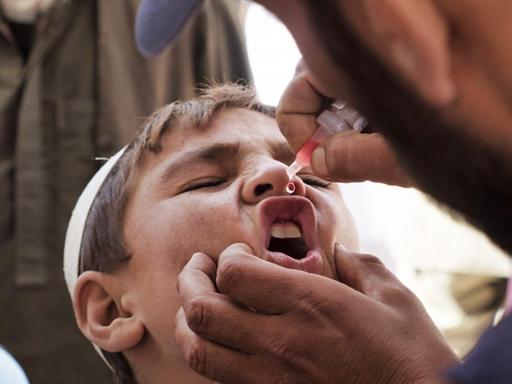 Ein Junge in Afghanistan wird von UNICEF-Mitarbeitern gegen Polio geimpft. Er bekommt den Tropfen aus der Pipette gerade in den Mund.