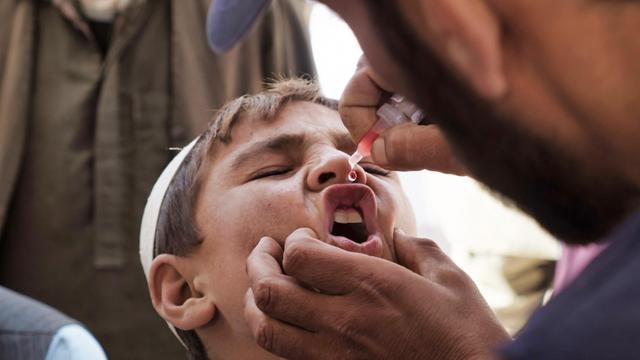 Ein Junge in Afghanistan wird von UNICEF-Mitarbeitern gegen Polio geimpft. Er bekommt den Tropfen aus der Pipette gerade in den Mund.
