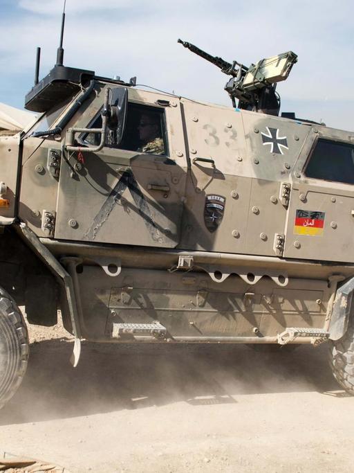 Ein gepanzertes Fahrzeug mit aufgedruckter Deutschlandfahne fährt durch staubige Landschaft