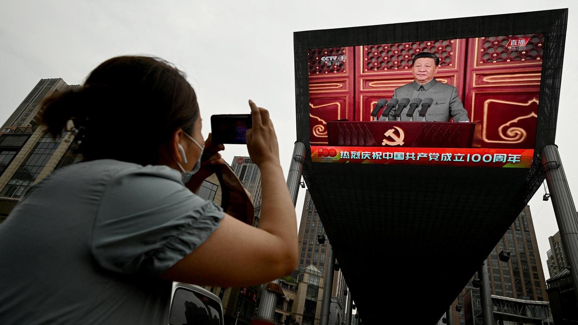 Eine Frau fotografiert eine Rede vom chinesischen Präsidenten Xi Jinping auf einem grossen Bildschirm auf der Strasse in Beijing während der 100-Jahres-Feier der kommunistischen Partei. China, 1.Juli 2021. Eine Frau fotografiert eine Rede vom chinesischen Präsidenten Xi Jinping auf einem grossen Bildschirm auf der Strasse in Beijing während der 100-Jahres-Feier der kommunistischen Partei. China, 1.Juli 2021.