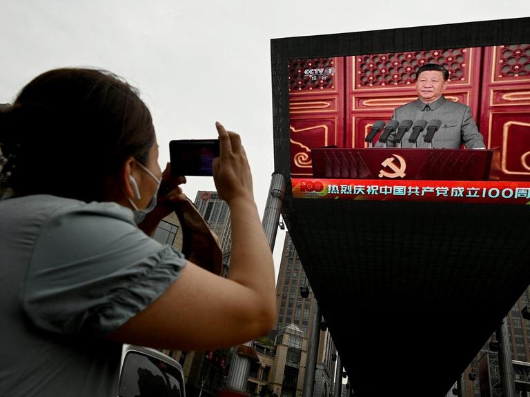 Eine Frau fotografiert eine Rede vom chinesischen Präsidenten Xi Jinping auf einem grossen Bildschirm auf der Strasse in Beijing während der 100-Jahres-Feier der kommunistischen Partei. China, 1.Juli 2021.