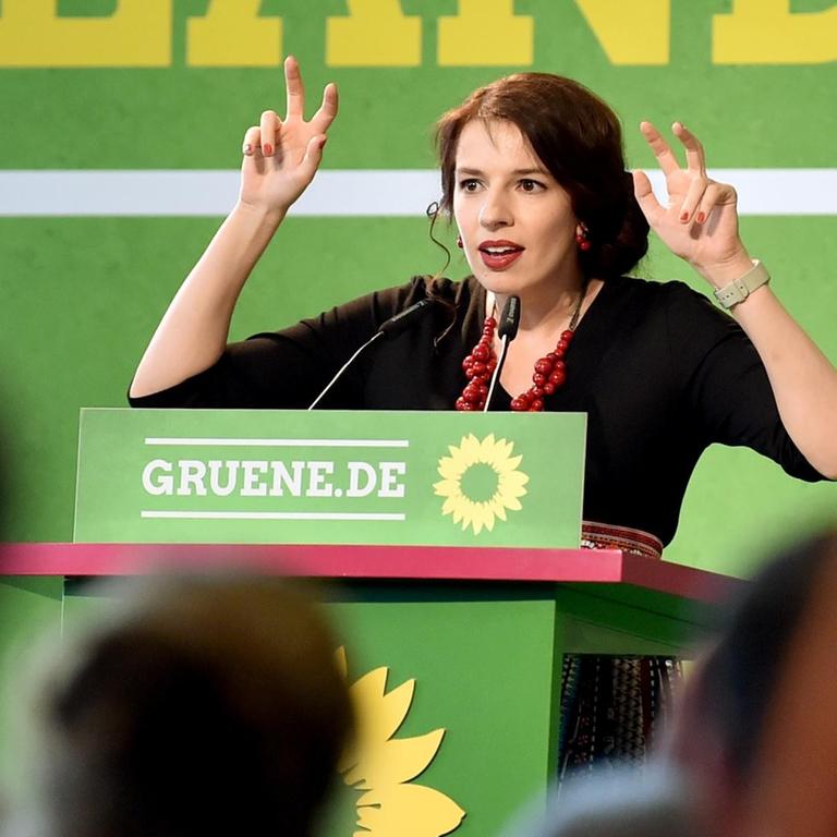 Marina Weisband steht auf einer Bühne und vor einem Pult mit dem Logo der Grünen und macht mit beiden Händen die Geste von Anführungsstrichen.