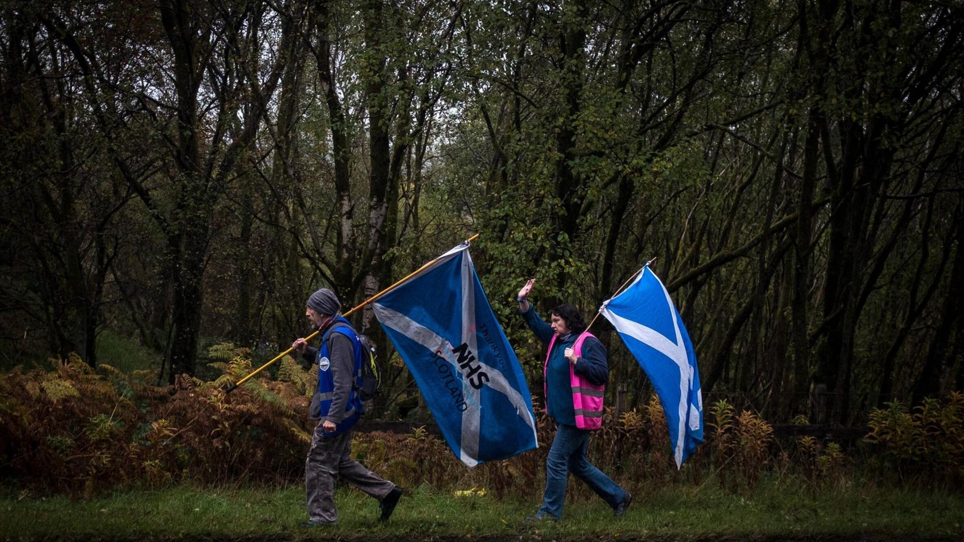 Ein Mann und eine Frau laufen mit Schottland-Flaggen an einem Waldstück entlang, 18. September 2020 Ein Mann und eine Frau laufen mit Schottland-Flaggen an einem Waldstück entlang, 18. September 2020