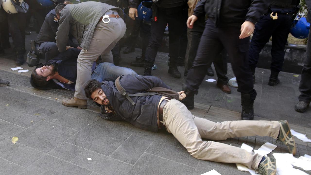 Polizisten fesseln auf dem Boden liegende Demonstranten.