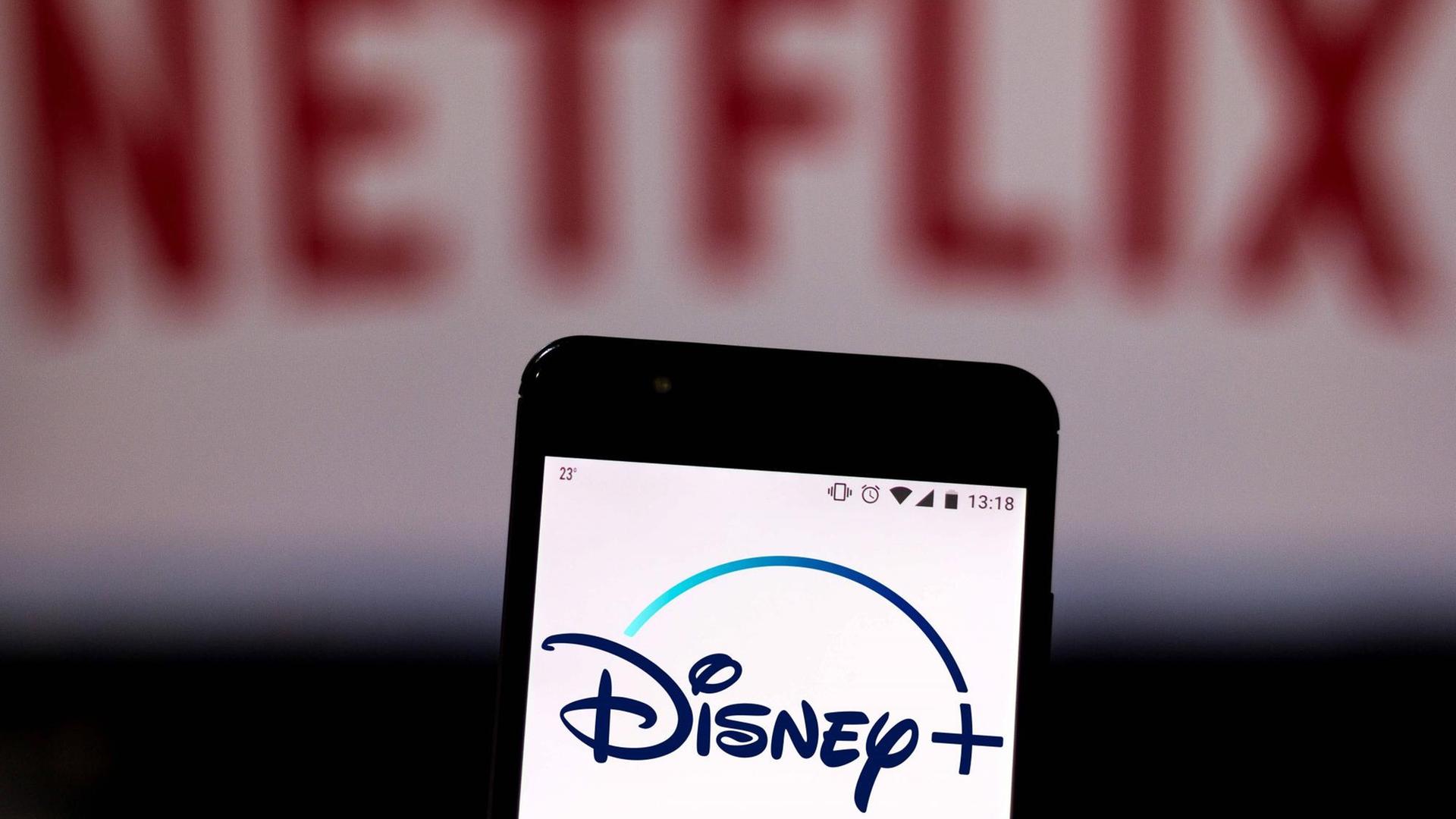 Auf einem Handy leuchtet das Logo von Disney+, im Hintergrund verschwommen das Netflix-Logo. Auf einem Handy leuchtet das Logo von Disney+, im Hintergrund verschwommen das Netflix-Logo.