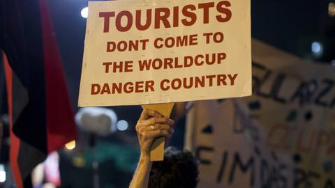 Eine ältere Frau hebt ein Schild in die Höhe, auf dem steht "Tourists, don't come to the worldcup danger country" - "Touristen, kommt nicht ins WM-Gefahren-Land"