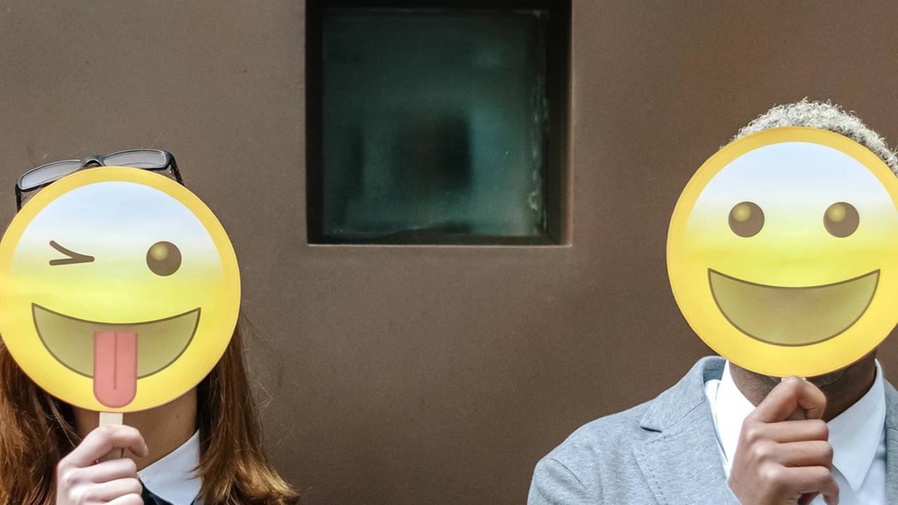 Eine Frau und ein Mann verdecken ihre Gesicher mit Emoji-Masken Eine Frau und ein Mann verdecken ihre Gesicher mit Emoji-Masken