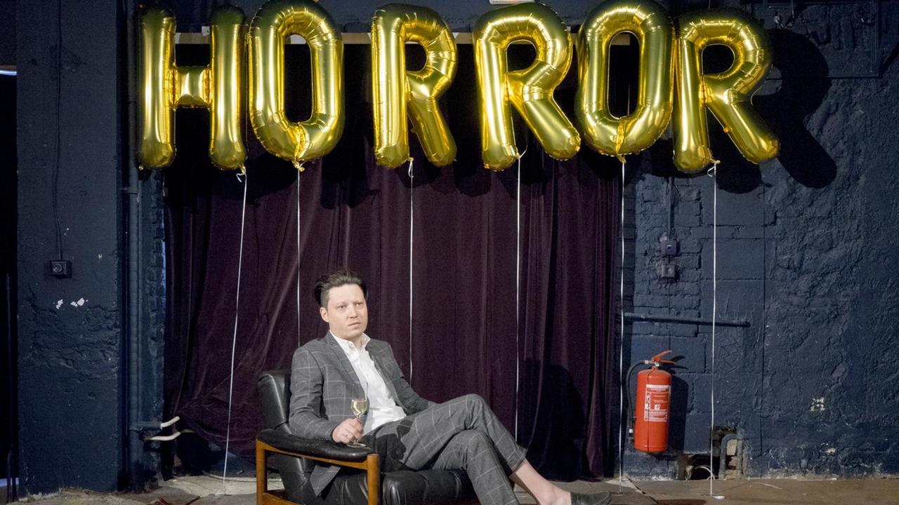 Ein Mann sitz in einem Schaukelstuhl. Hinter ihm der Schriftzug Horror aus Ballons. Ein Mann sitz in einem Schaukelstuhl. Hinter ihm der Schriftzug Horror aus Ballons.