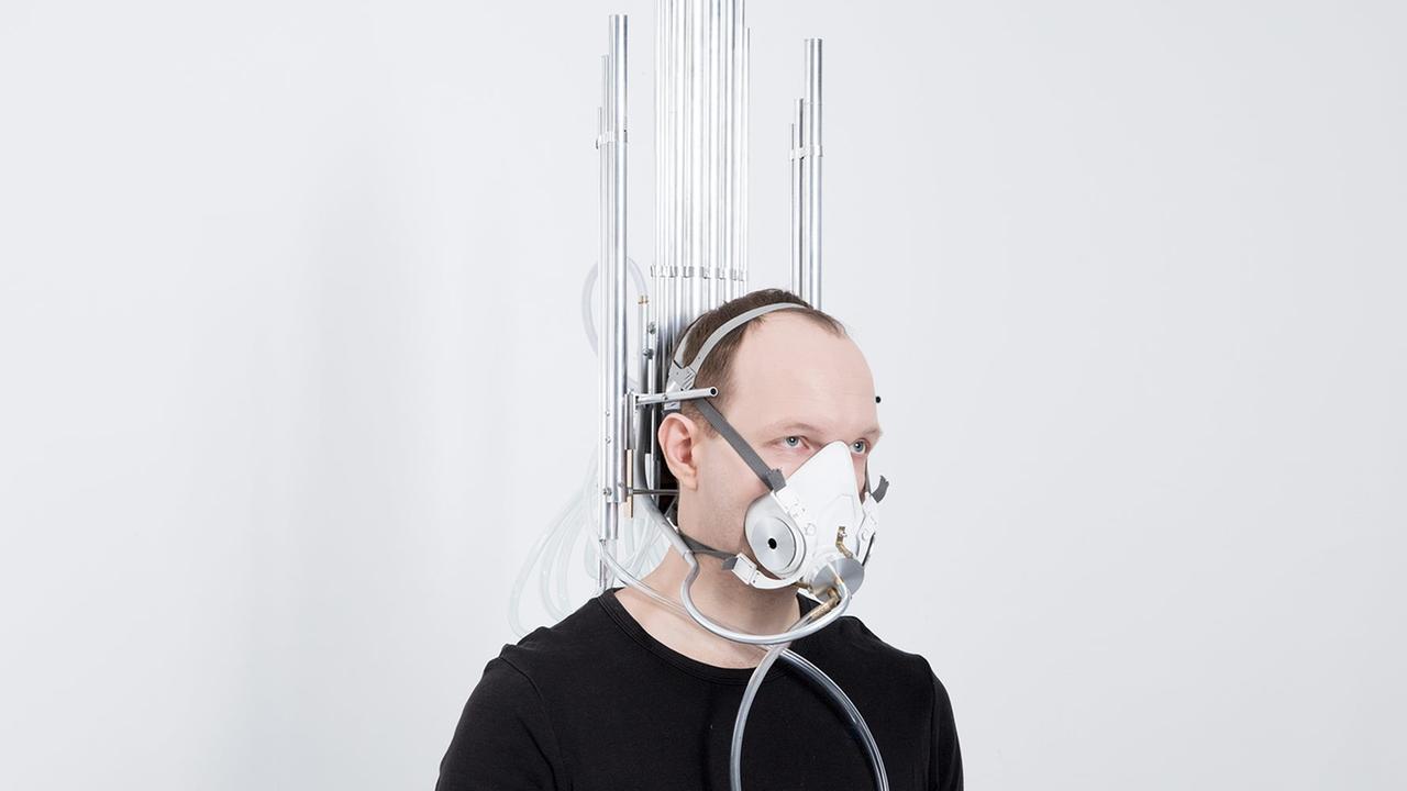 Ein Mann steht mit Atemmaske vor einer futuristischen Wandinstallation in einem weißen Raum. Es handelt sich um ein Kunstwerk des russischen Künstlers Dmitry Morozov mit dem Titel "Last Breath". Ein Mann steht mit Atemmaske vor einer futuristischen Wandinstallation in einem weißen Raum. Es handelt sich um ein Kunstwerk des russischen Künstlers Dmitry Morozov mit dem Titel "Last Breath".
