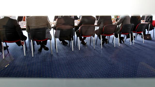 Eine Gruppe Männer mit Anzügen sitzen in einem Konferenzraum.