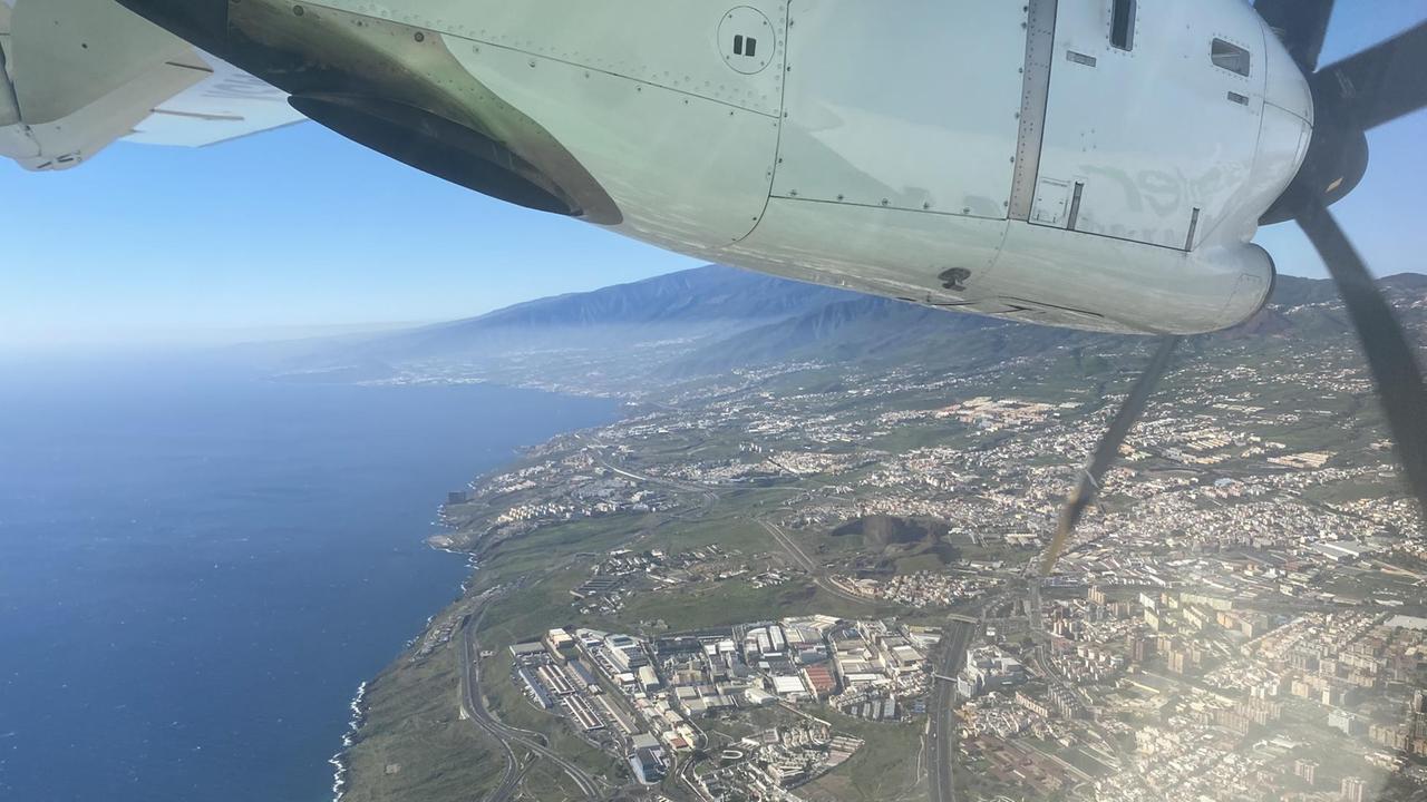 Eine Insel im Meer weit unten schaut unter einem Flugzeugflügel hervor. Eine Insel im Meer weit unten schaut unter einem Flugzeugflügel hervor.