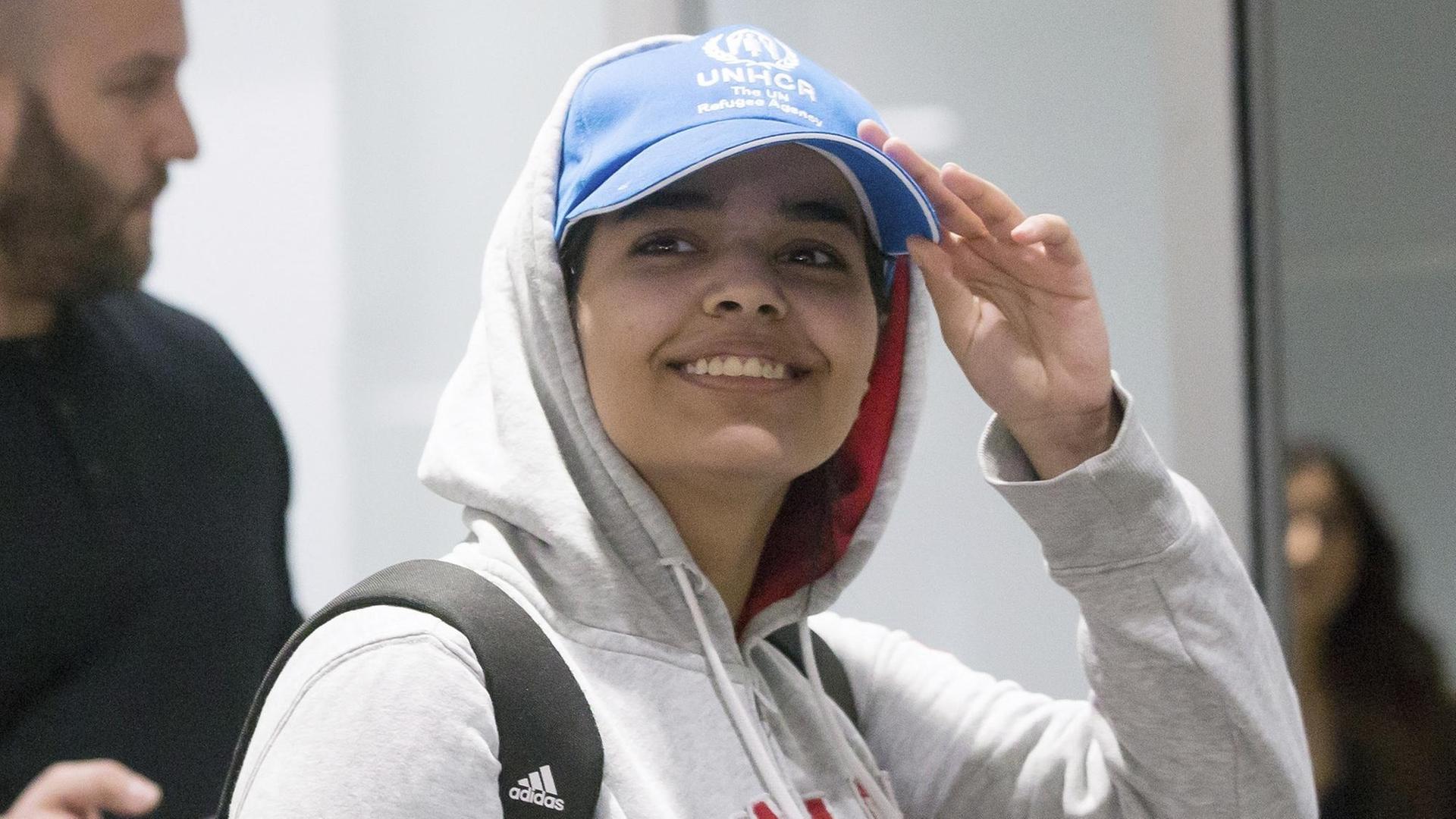 Die junge Frau trägt ein graues Sweat-Shirt mit der Aufschrift "Kanada" und eine blaue Baseball-Cap des UNHCR. Sie lächelt breit und greift an den Schirm ihrer Mütze. Die junge Frau trägt ein graues Sweat-Shirt mit der Aufschrift "Kanada" und eine blaue Baseball-Cap des UNHCR. Sie lächelt breit und greift an den Schirm ihrer Mütze.