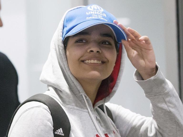 Die junge Frau trägt ein graues Sweat-Shirt mit der Aufschrift "Kanada" und eine blaue Baseball-Cap des UNHCR. Sie lächelt breit und greift an den Schirm ihrer Mütze.
