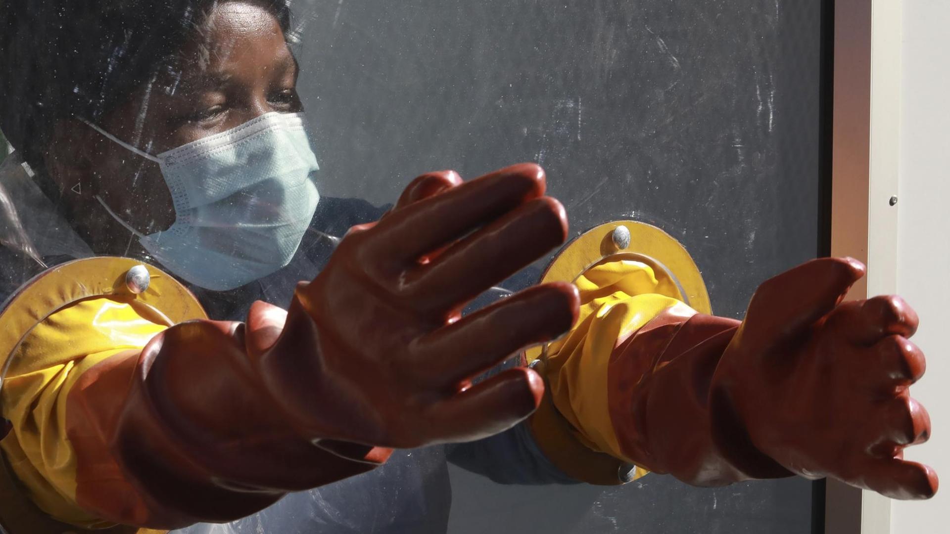 Im südafrikanischen Kapstadt ist eine Mitarbeiterin des Gesundheitswesens hinter einer Plastikscheibe mit darin angebrachten Gummihandschuhen zu sehen. Im südafrikanischen Kapstadt ist eine Mitarbeiterin des Gesundheitswesens hinter einer Plastikscheibe mit darin angebrachten Gummihandschuhen zu sehen.