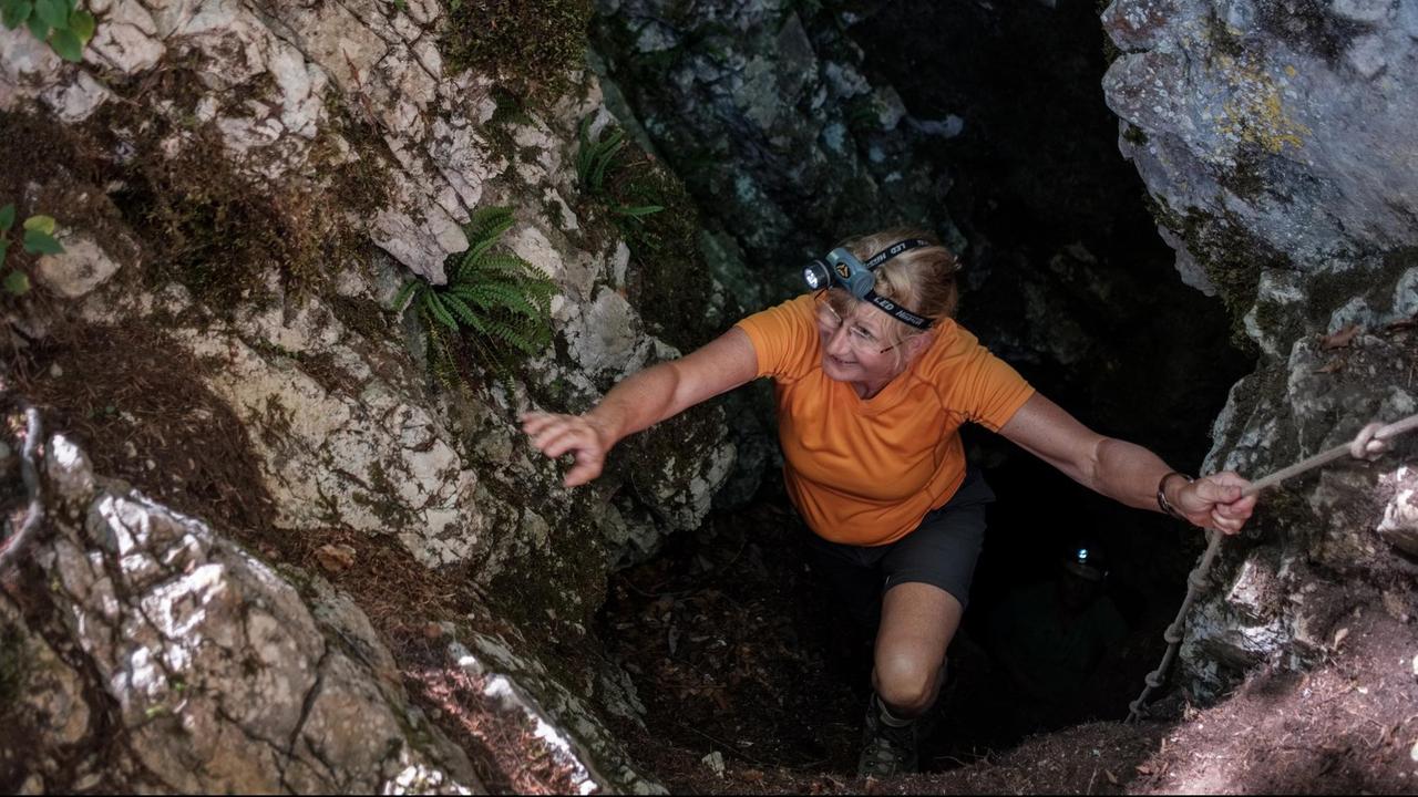 Eine Wandererin klettert in eine Tropfsteinhöhle