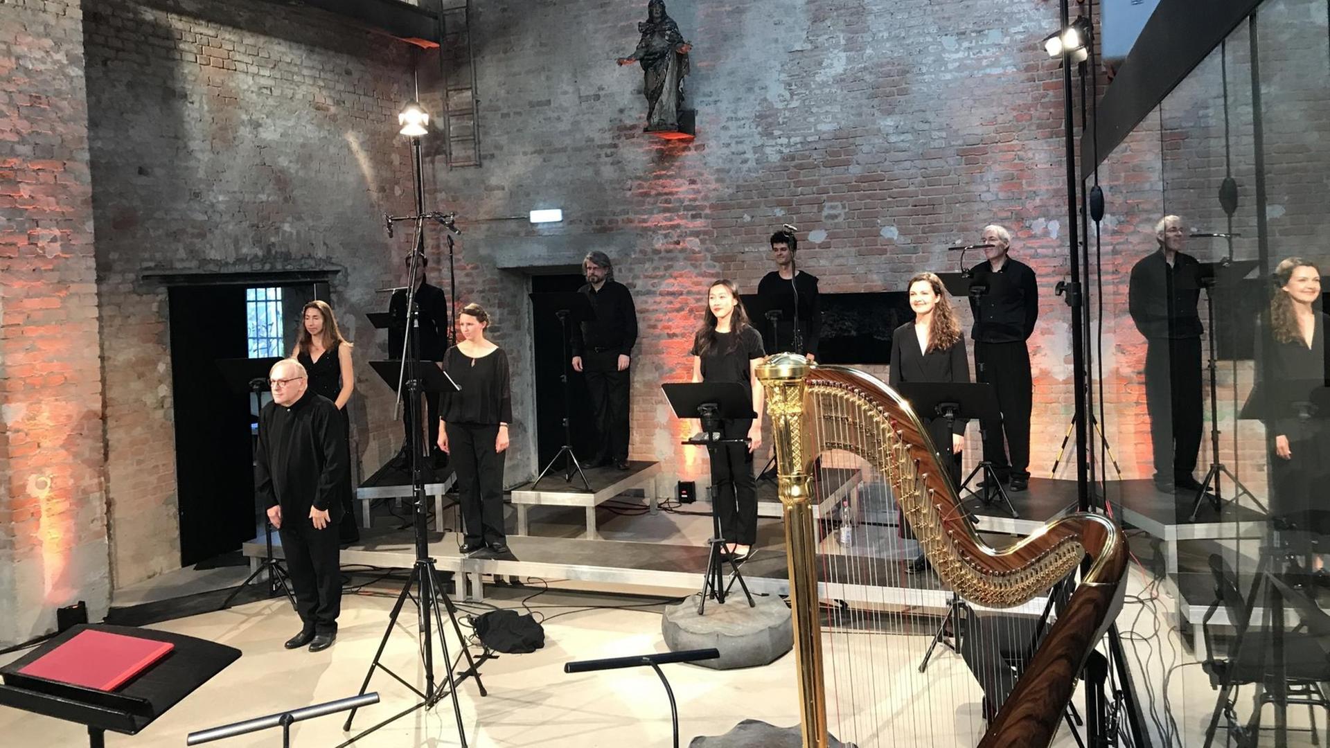 In einer Kirche steht eine Gruppe von schwarz gekleideten Musikerinnen und Musikern zum Konzert zusammen. Im Vordergrund ist eine Harfe zu sehen. In einer Kirche steht eine Gruppe von schwarz gekleideten Musikerinnen und Musikern zum Konzert zusammen. Im Vordergrund ist eine Harfe zu sehen.