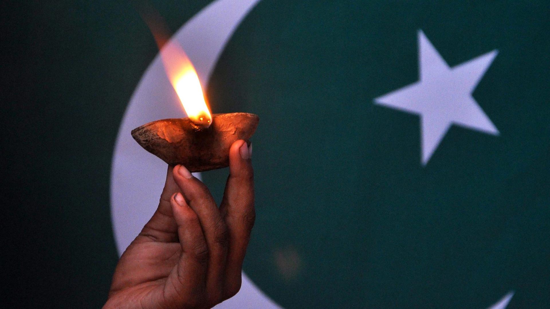 Eine Kinderhand hält eine Lampe vor der pakistanischen Flagge. Eine Kinderhand hält eine Lampe vor der pakistanischen Flagge.