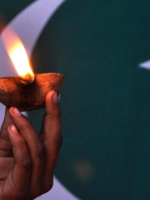 Eine Kinderhand hält eine Lampe vor der pakistanischen Flagge.