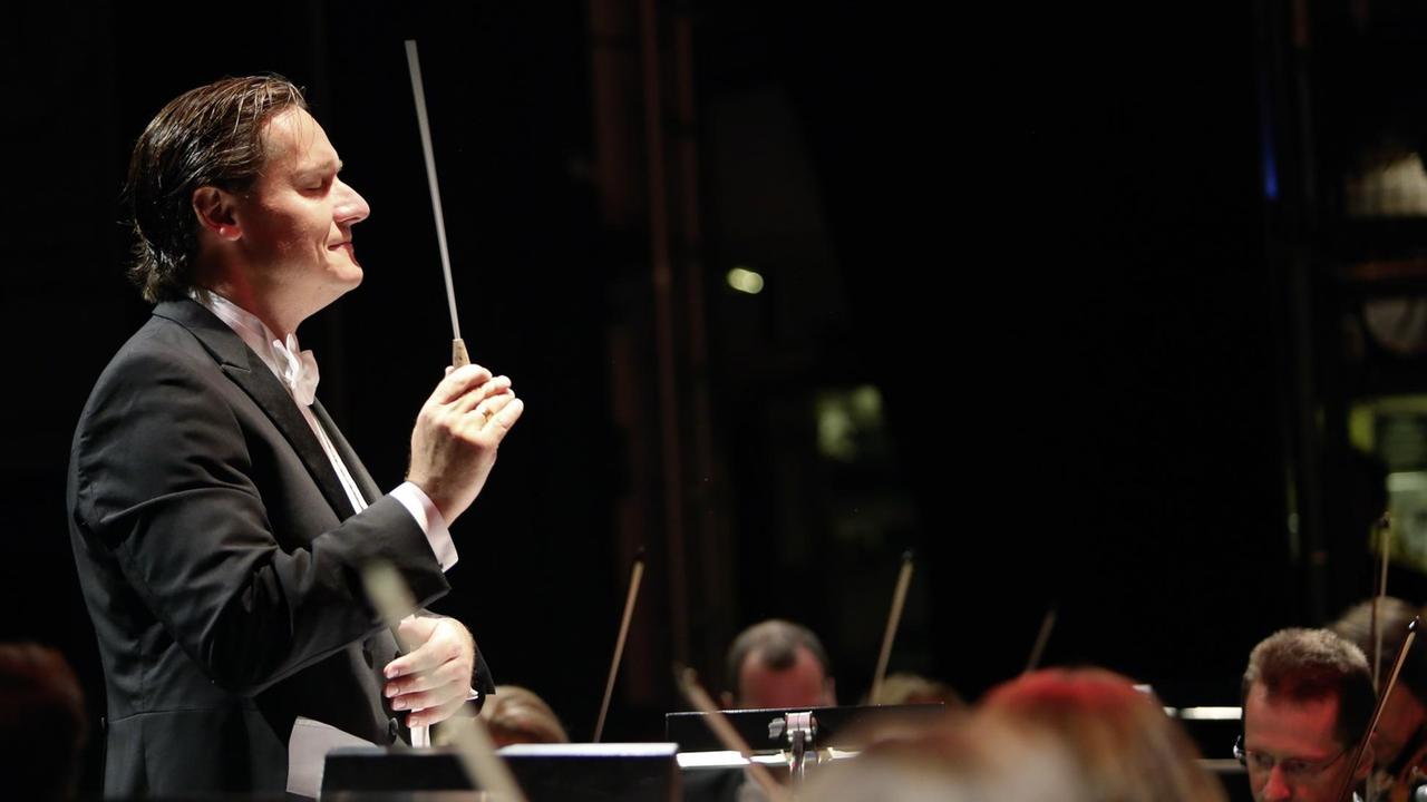 Der Dirigent Stefan Klingele steht vor einem Orchester und gibt den Einsatz