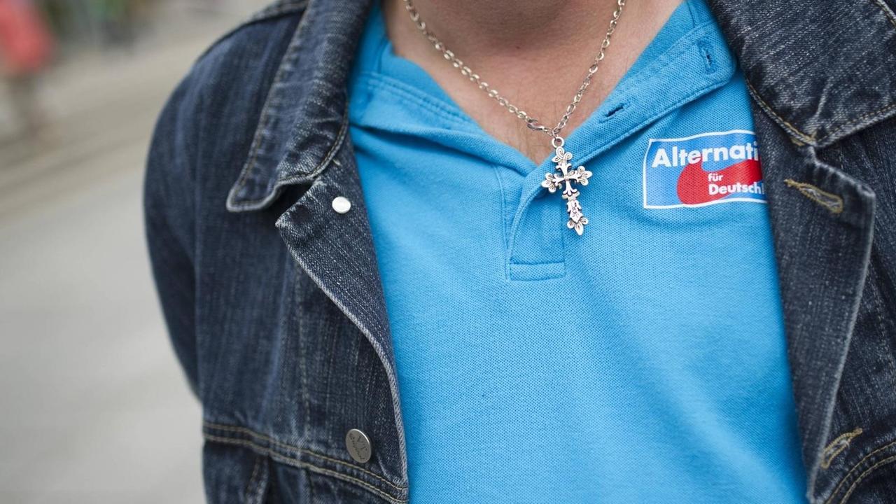 Ein Besucher einer Wahlveranstaltung der Partei Alternative für Deutschland (AfD) trägt eine Kette mit einem Kreuz und ein blaues T-Shirt mit dem Logo der AfD. Ein Besucher einer Wahlveranstaltung der Partei Alternative für Deutschland (AfD) trägt eine Kette mit einem Kreuz und ein blaues T-Shirt mit dem Logo der AfD.