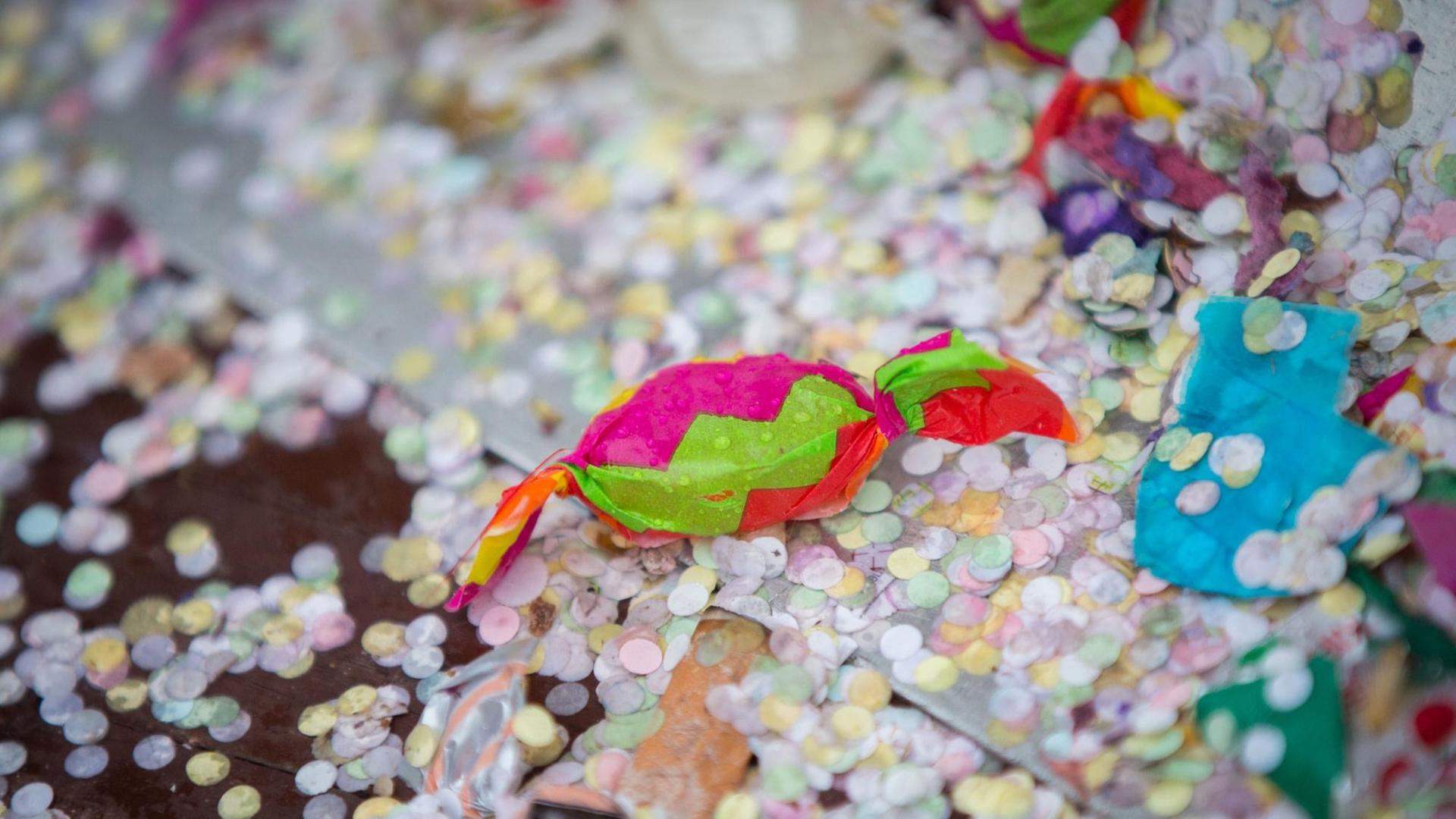 Ein Bonbon von einem Karnevalsumzug liegt zwischen nassem Konfetti auf der Straße Ein Bonbon von einem Karnevalsumzug liegt zwischen nassem Konfetti auf der Straße