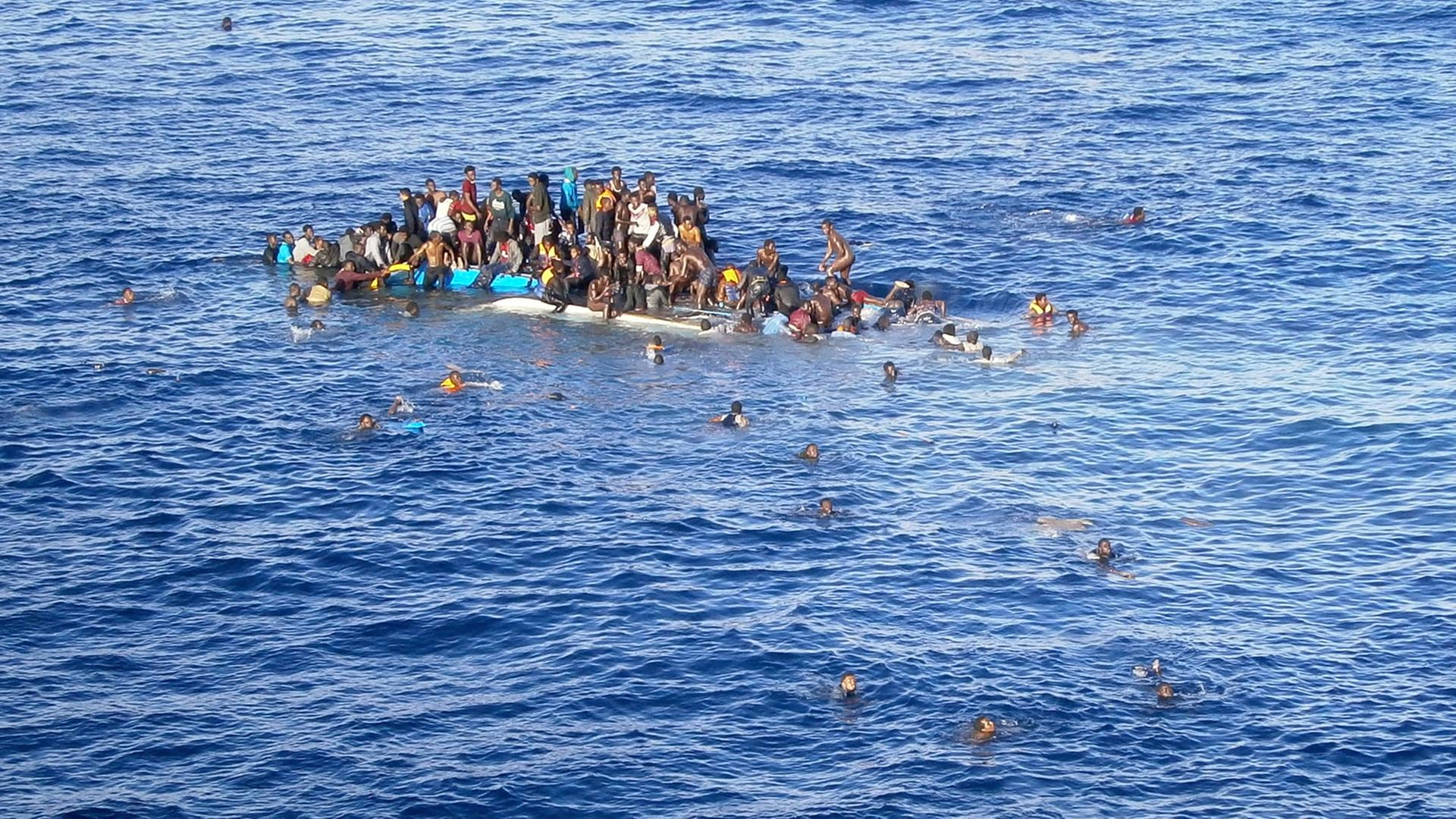 Die Aufnahme zeigt Flüchtlinge, die mit ihrem Boot in unmittelbarer Nähe eines Frachtschiffes auf dem Mittelmeer gekentert sind.