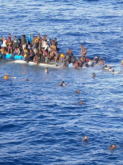 Die Aufnahme zeigt Flüchtlinge, die mit ihrem Boot in unmittelbarer Nähe eines Frachtschiffes auf dem Mittelmeer gekentert sind.