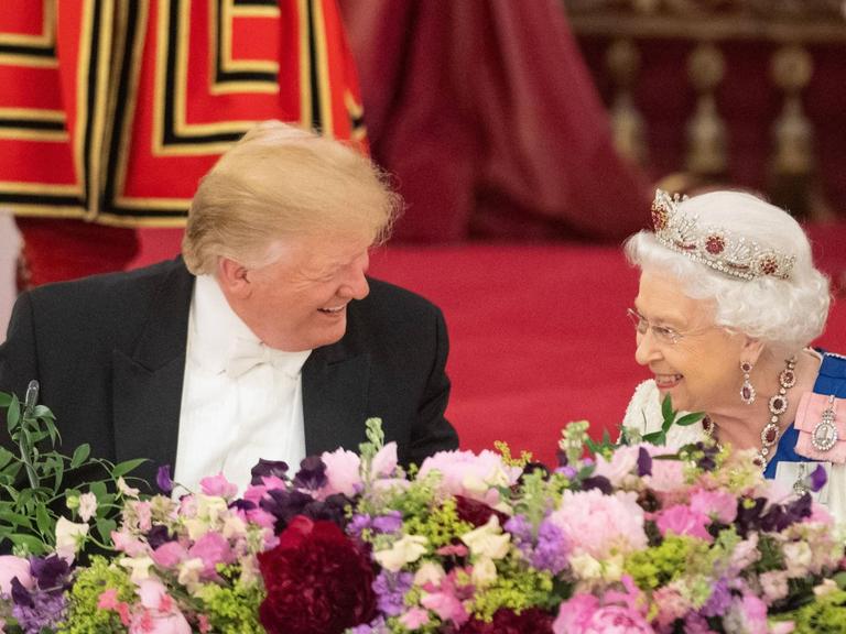 Donald Trump sitzt lachend beim Staatsbankett neben der britischen Königin. Auch die Queen lächelt.