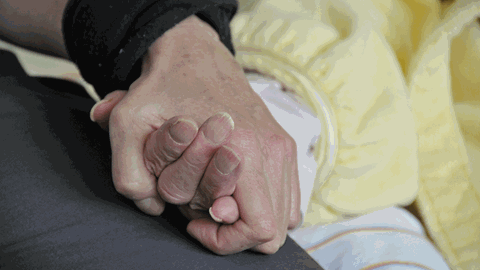 Eine Tochter hält die Hand ihrer Mutter im Krankenhaus.