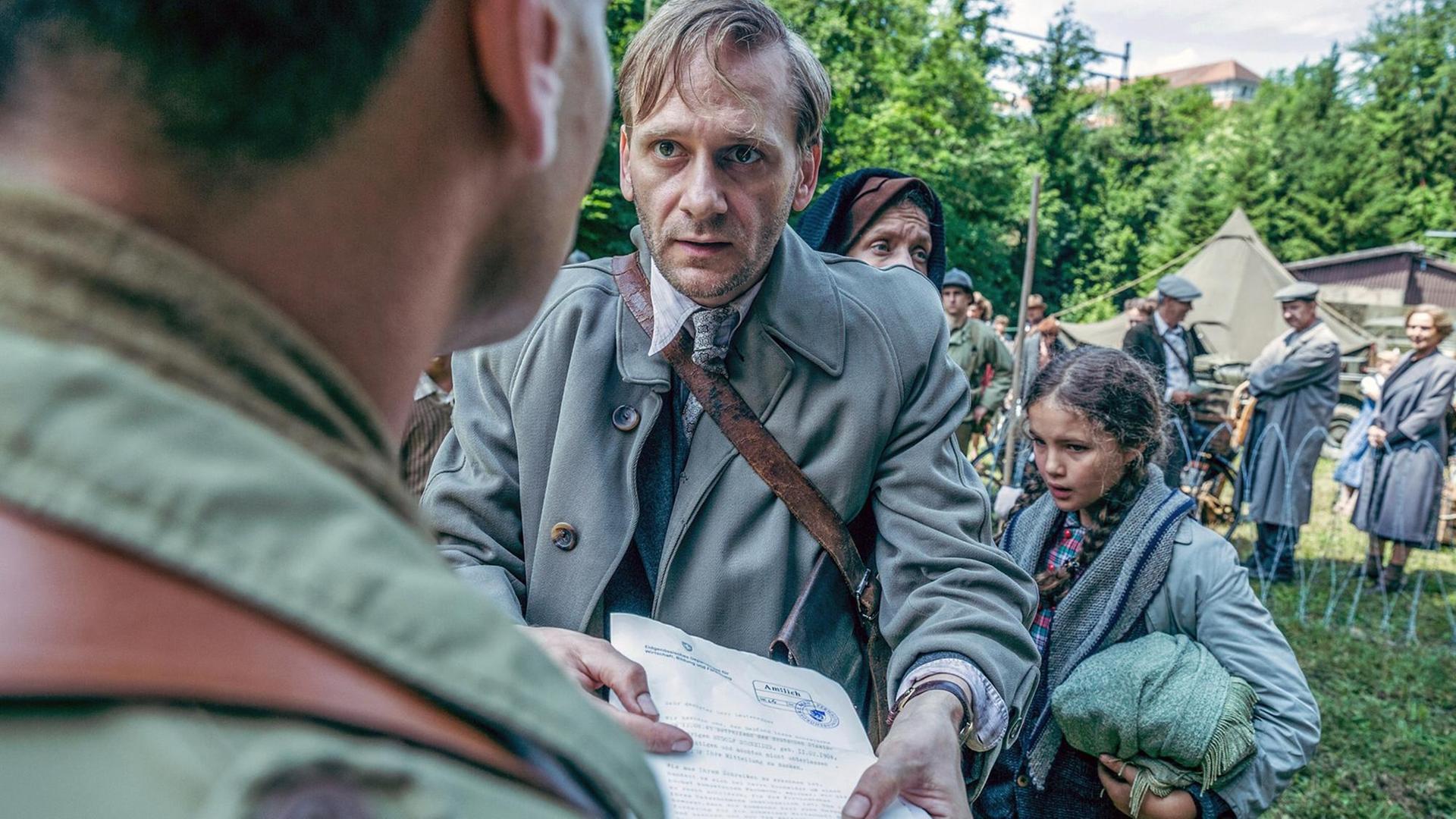 Ein Mann hält mit ängstlichem Gesichtsausdruck einem Uniformierten ein amtliches Dokument entgegen. Ein Mann hält mit ängstlichem Gesichtsausdruck einem Uniformierten ein amtliches Dokument entgegen.